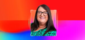 Smiling professional woman with long dark hair and glasses, wearing a green patterned top, photographed against a vibrant red, pink and blue gradient background.